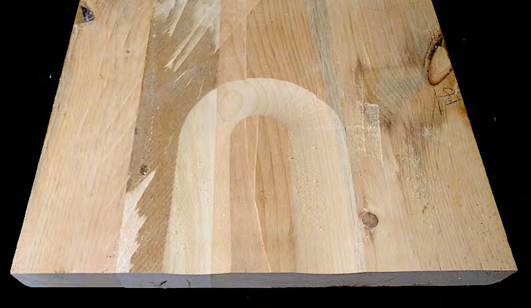 A Windsor chair seat blank with the saddle hollowed out, showing the arcs left by successive table-saw passes